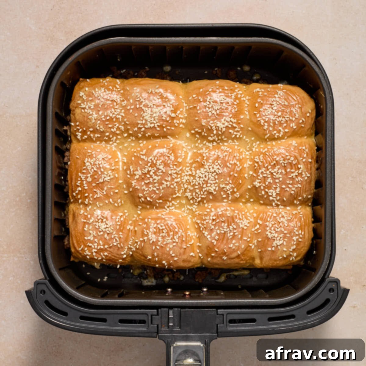 Air Fryer Mini Cheeseburgers 10 Sliders fully assembled in the air fryer basket with the melted butter mixture and sesame seeds on top.